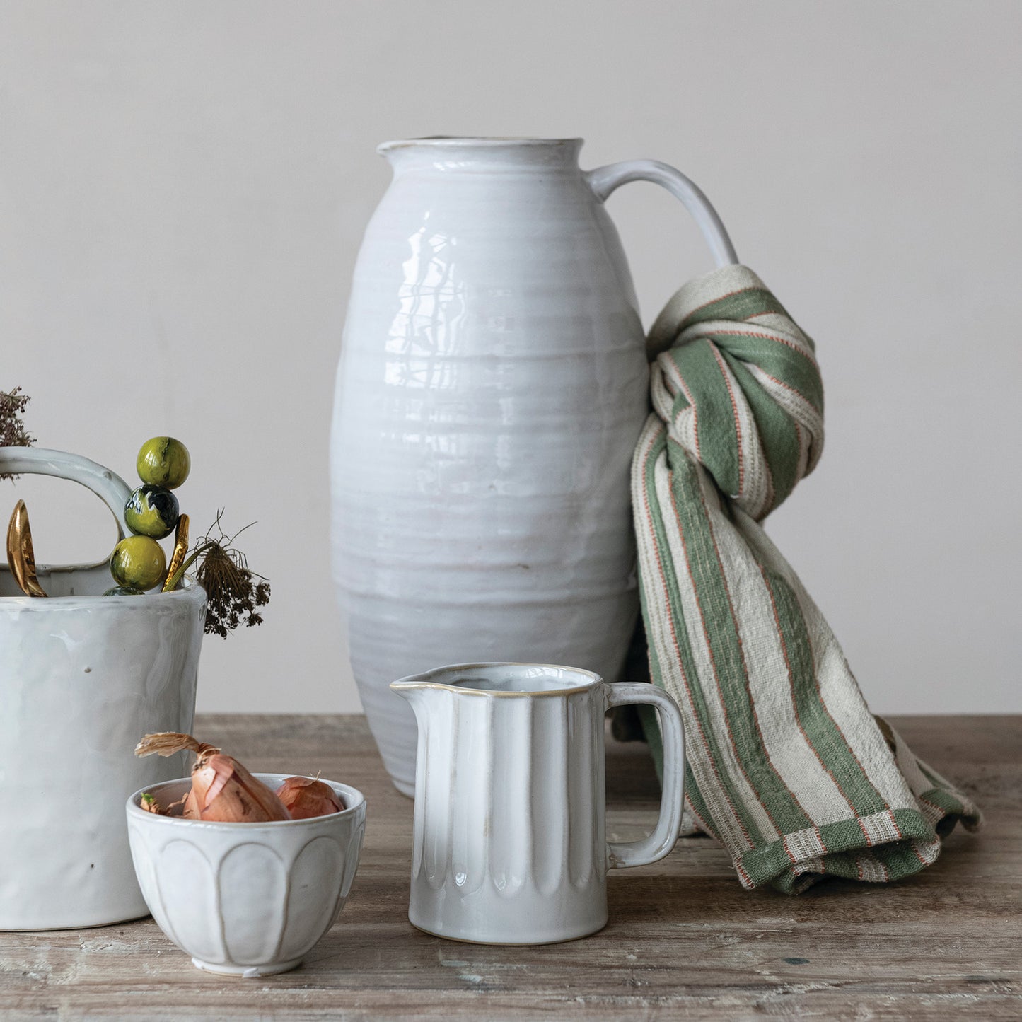 Set of ceramic items including a pitcher, bowl, and cup on a wooden surface with a striped towel.