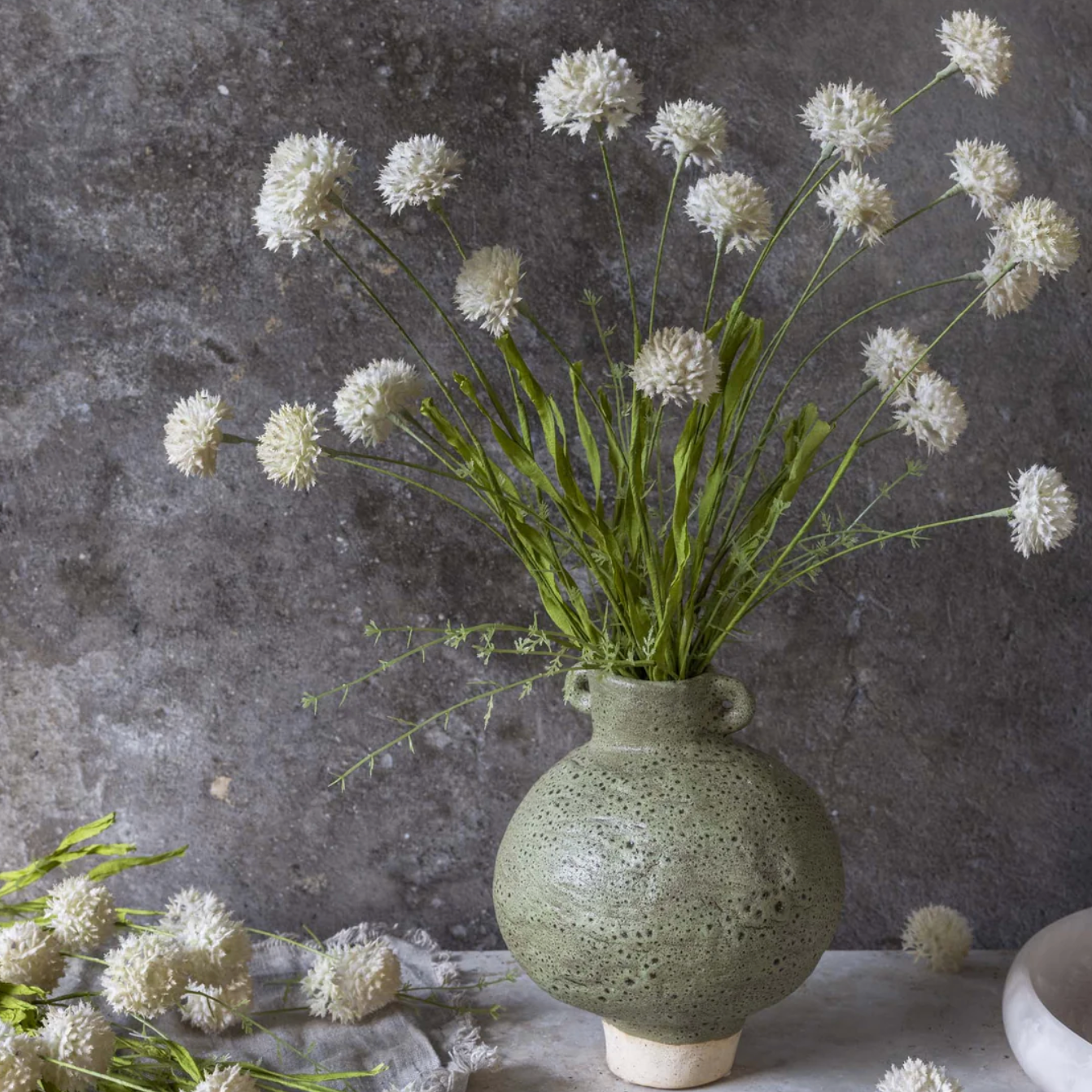 Green vase with white flowers against a gray textured wall 21" Artificial Melaleuca Cream Stem