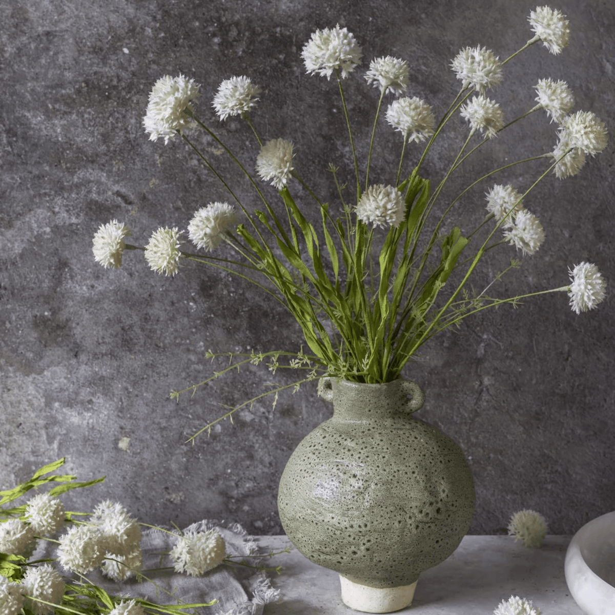 Green vase with white flowers against a gray textured wall 21" Artificial Melaleuca Cream Stem