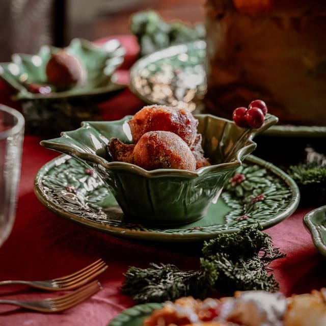Decorative table setting with green ceramic dishes and red berries on a red tablecloth.