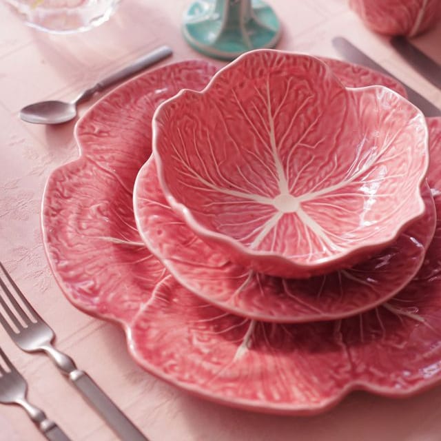 Pink cabbage leaf-patterned dinnerware set on a table with floral decorations.