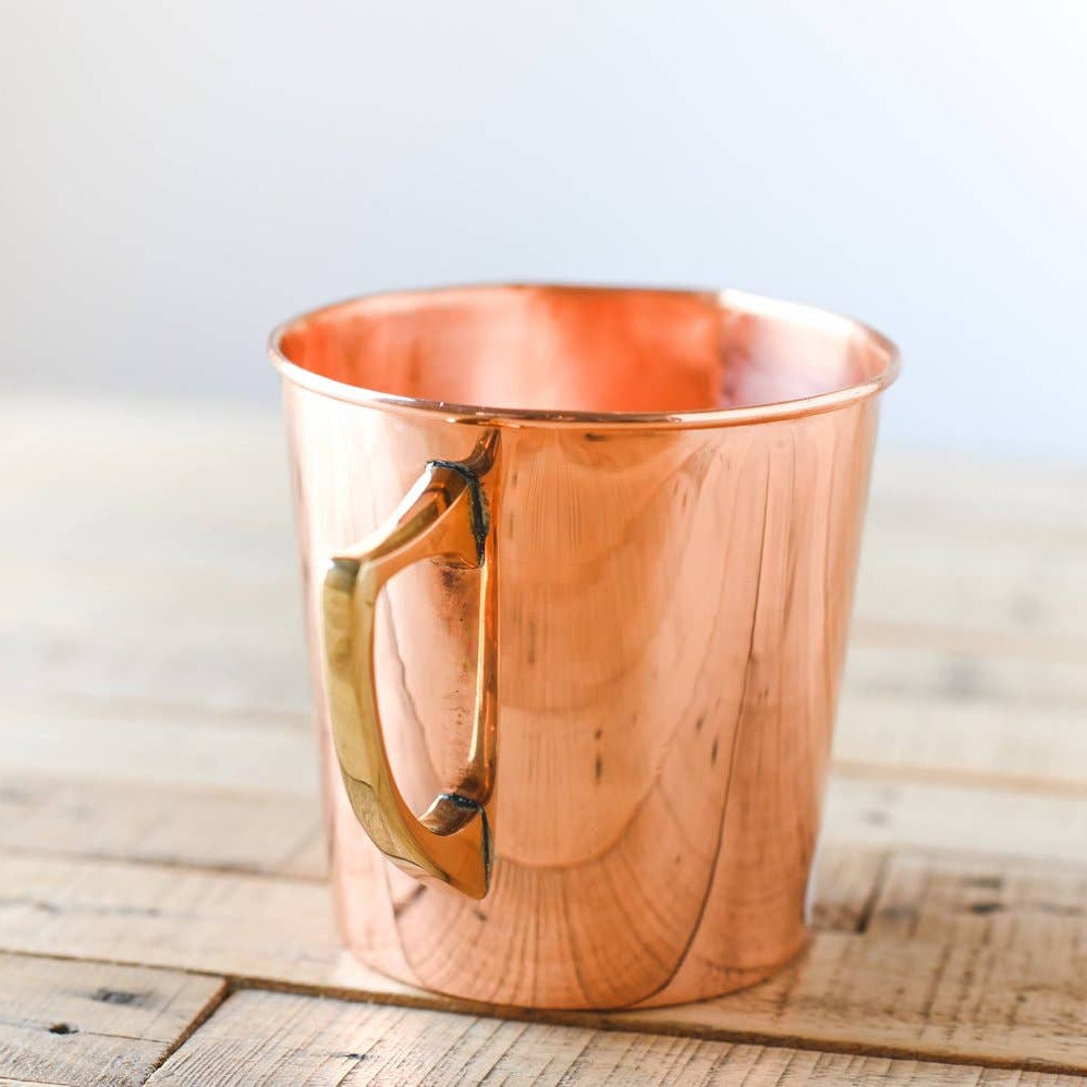 Copper measuring cup with gold handle on a textured surface