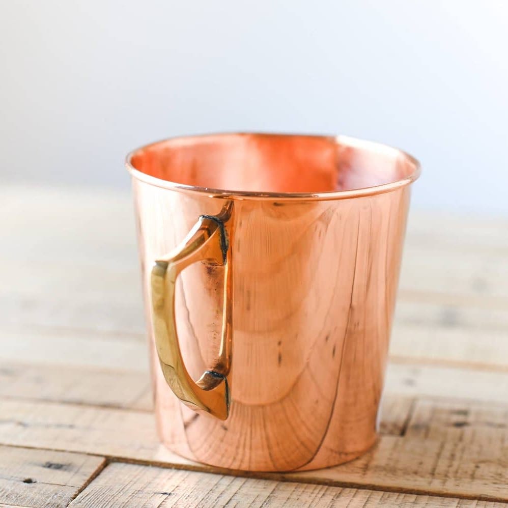 Copper measuring cup with gold handle on a textured surface