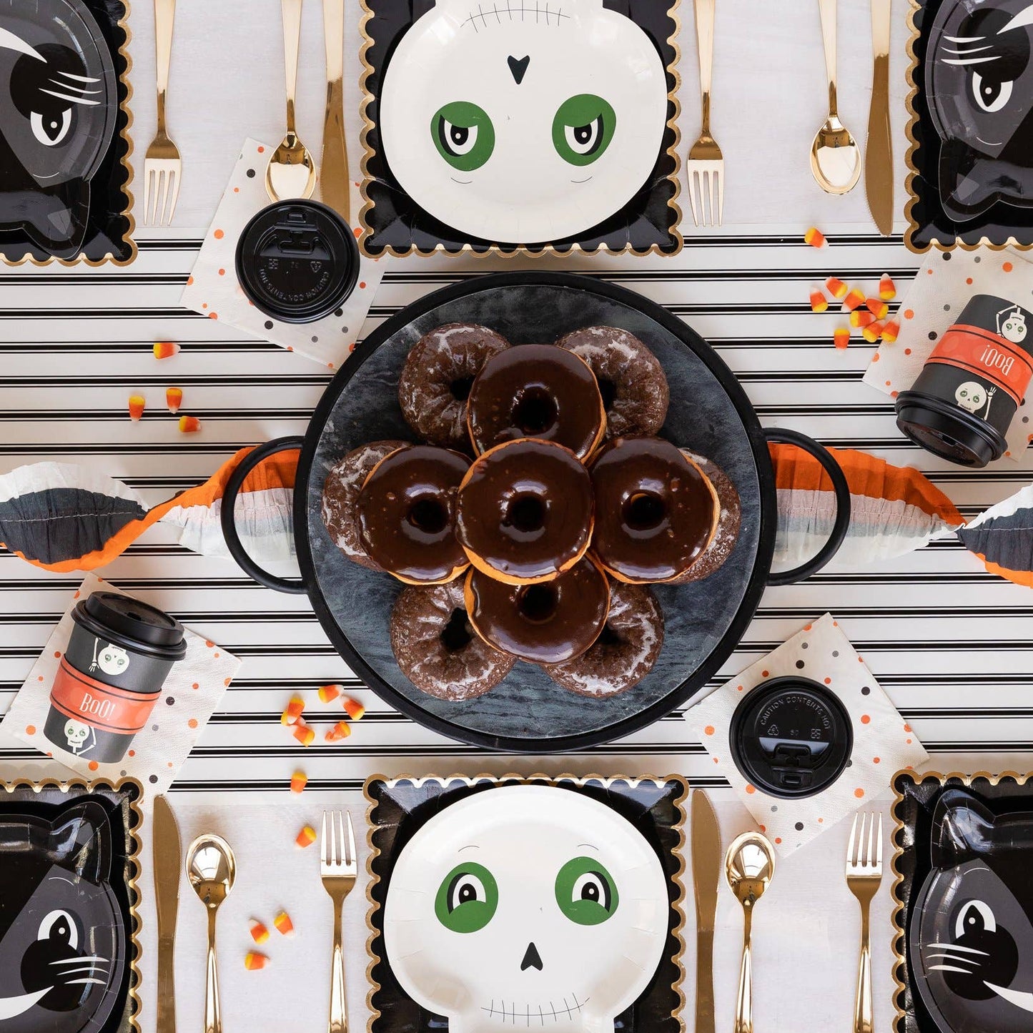 Halloween-themed table setting with black cat plates, donuts, and decorative items on a striped paper table runner.