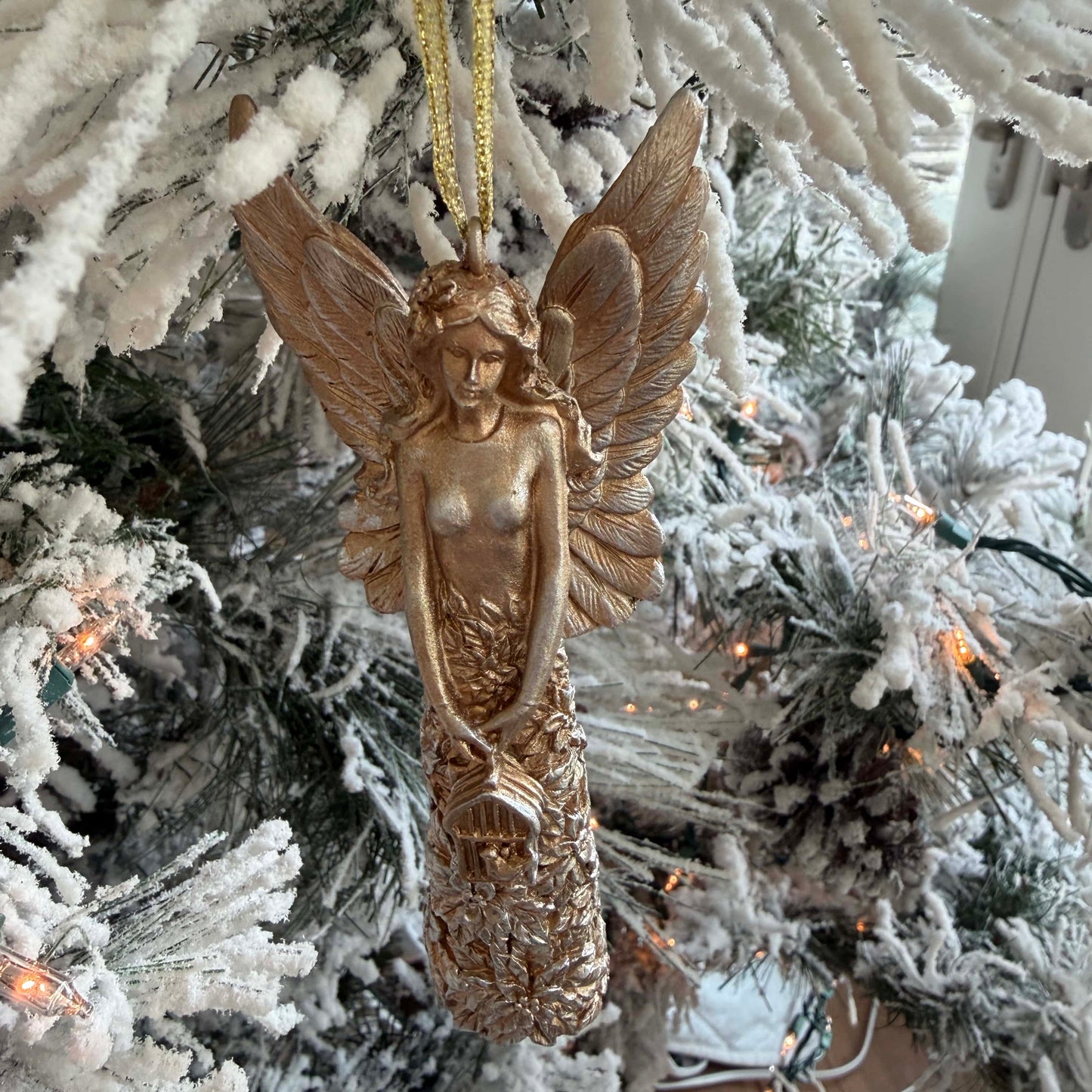 Gold angel ornament hanging on a snow-covered Christmas tree