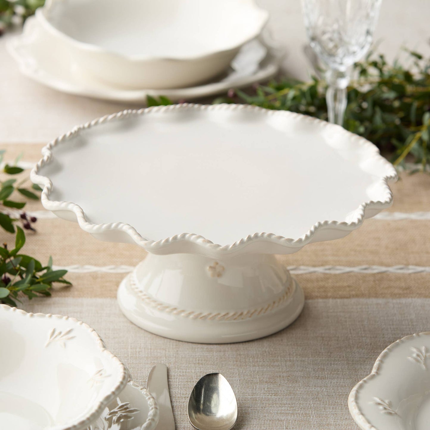 Decorative white ceramic dish on a table with greenery and cutlery