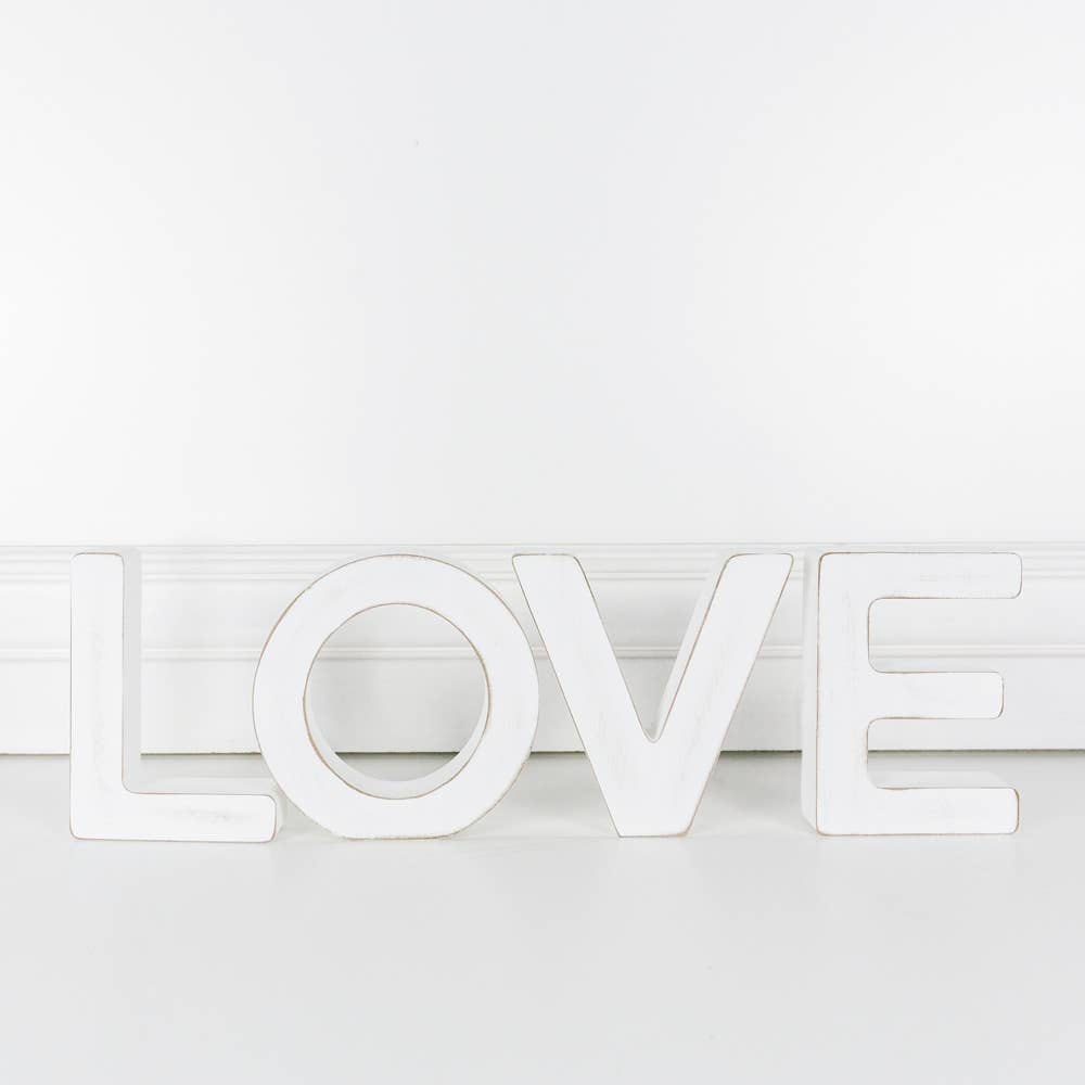A white wooden cutout letter 'L' with the word 'LOVE' made out of cutout letters, standing upright against a white background.