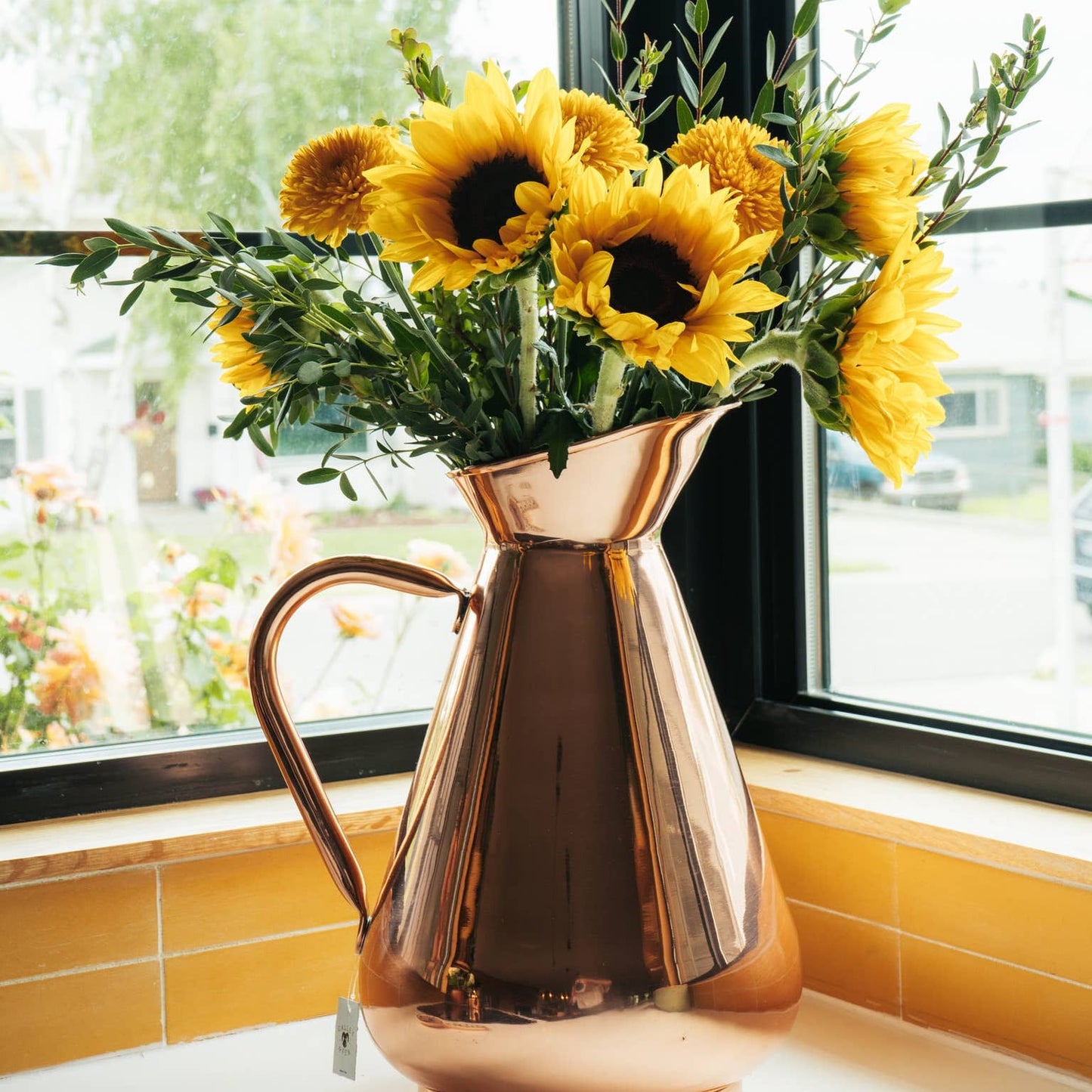 Copper pitcher filled with sunflowers on a windowsill