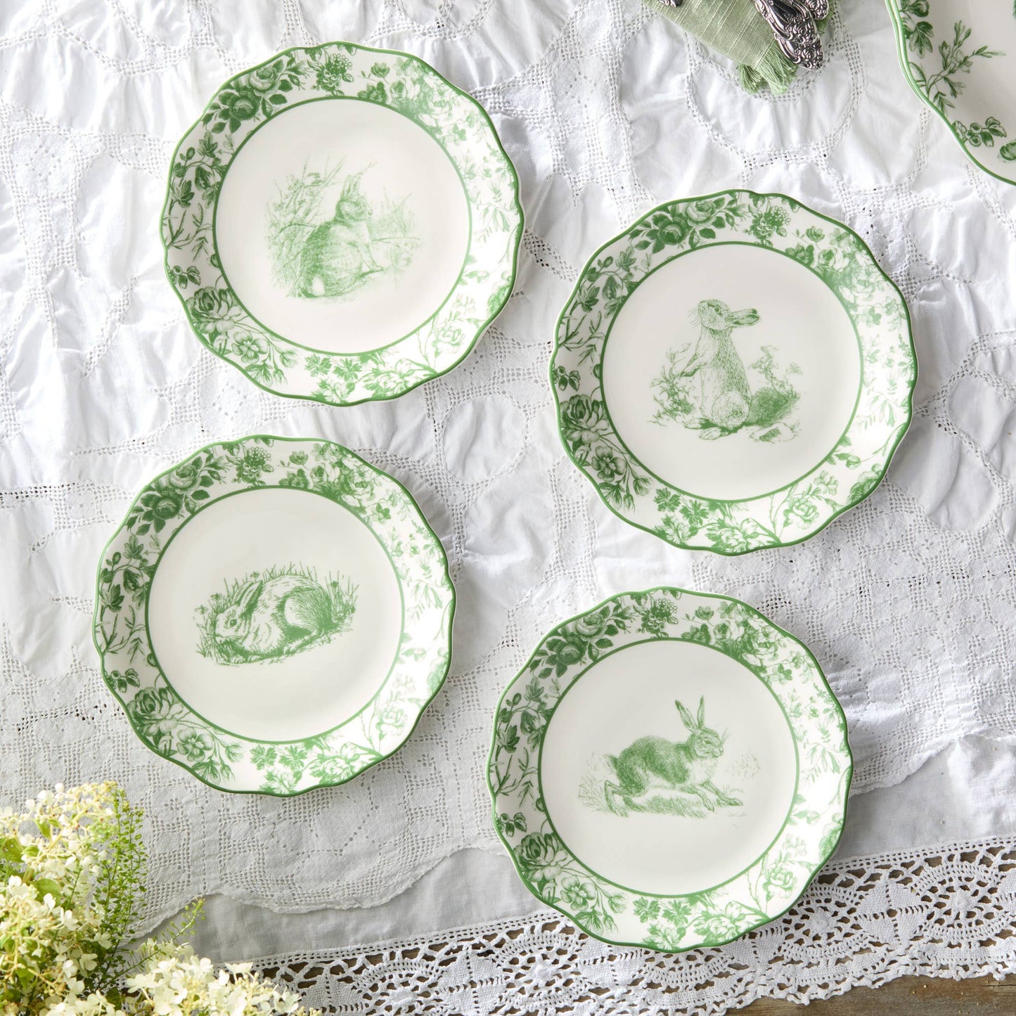 Set of four green and white decorative plates with animal illustrations on a lace tablecloth.