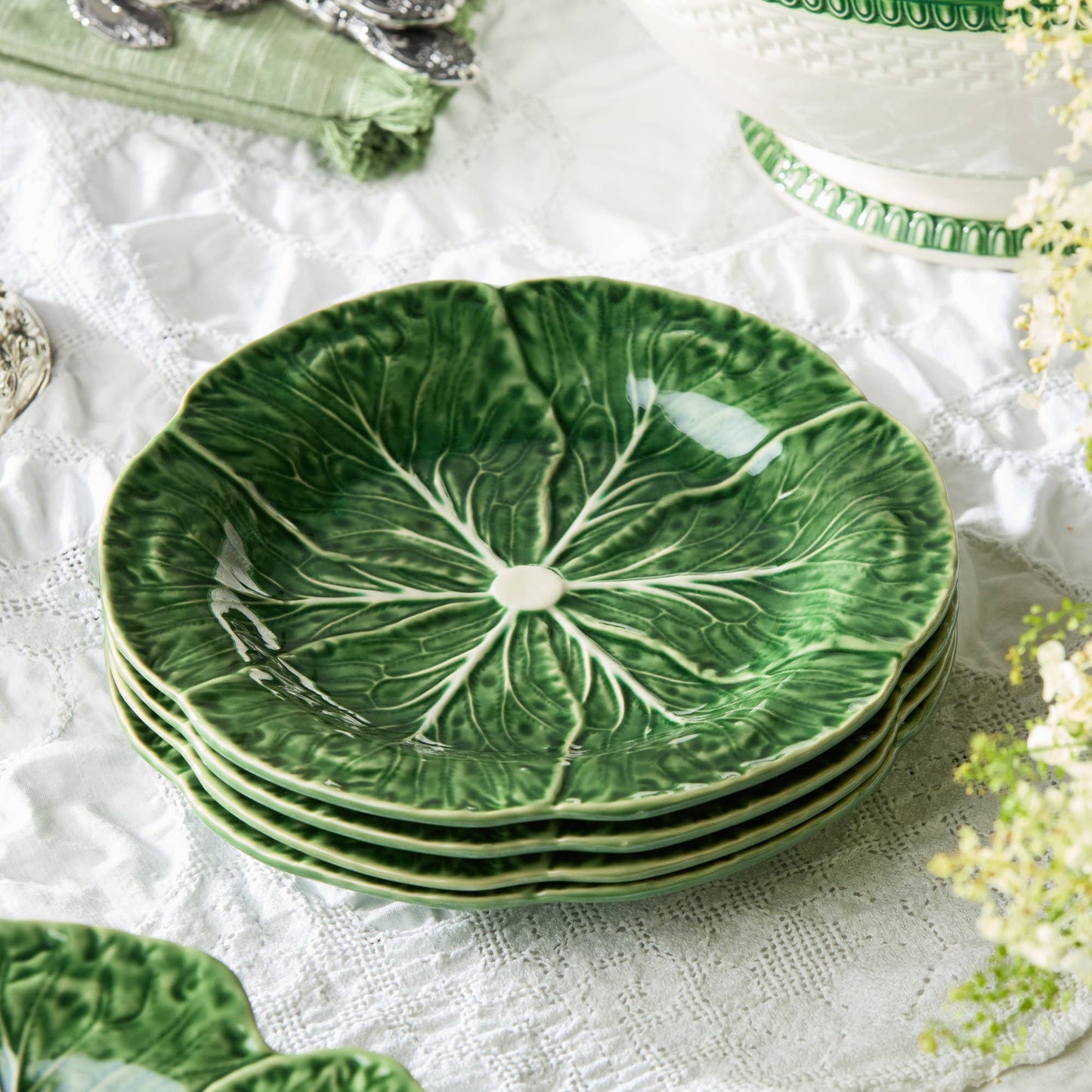 Set of green ceramic plates with leaf design on a white lace tablecloth.