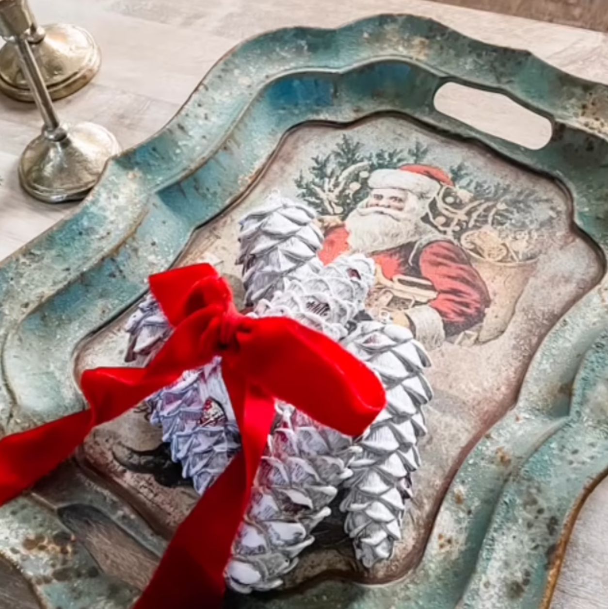 A decorative tray with a painted image of Santa Claus surrounded by presents, adorned with a red ribbon.