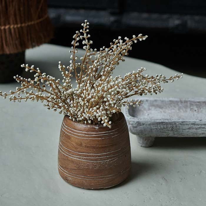 An arrangement of artificial heather in a cream color, displayed in a beige vase on a table.