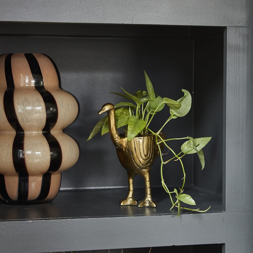 A bronze-colored aluminum decorative pot in the shape of an ostrich, with a small potted plant inside it, placed on a dark surface.