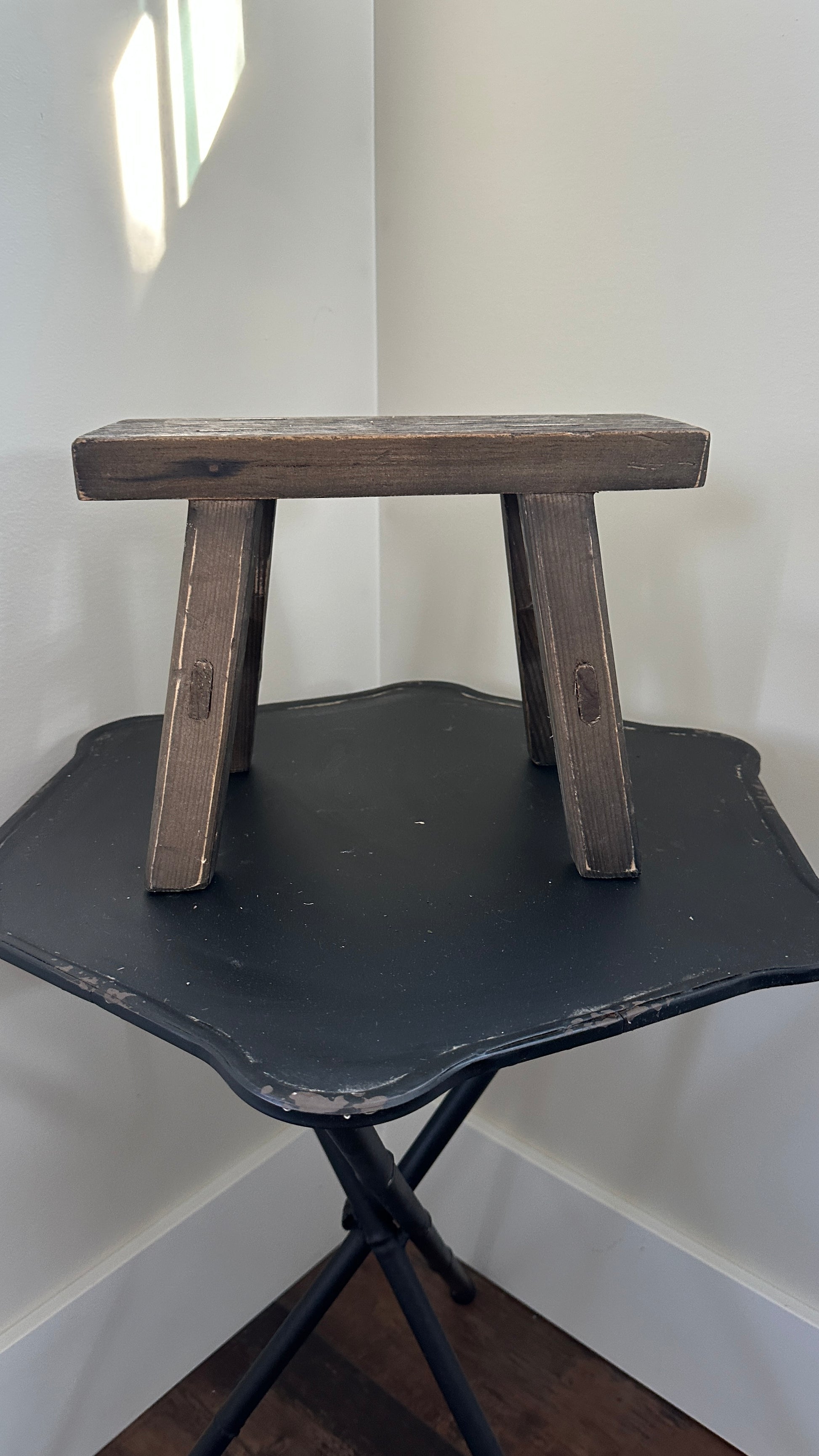Wooden step stool on a black folding table against a white wall.