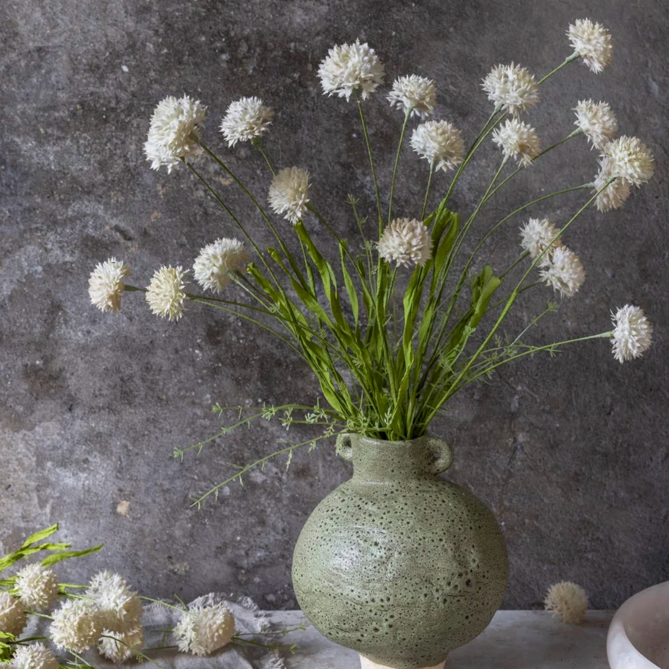 Green vase with white flowers against a dark textured wall 21" Artificial Melaleuca Cream Stem