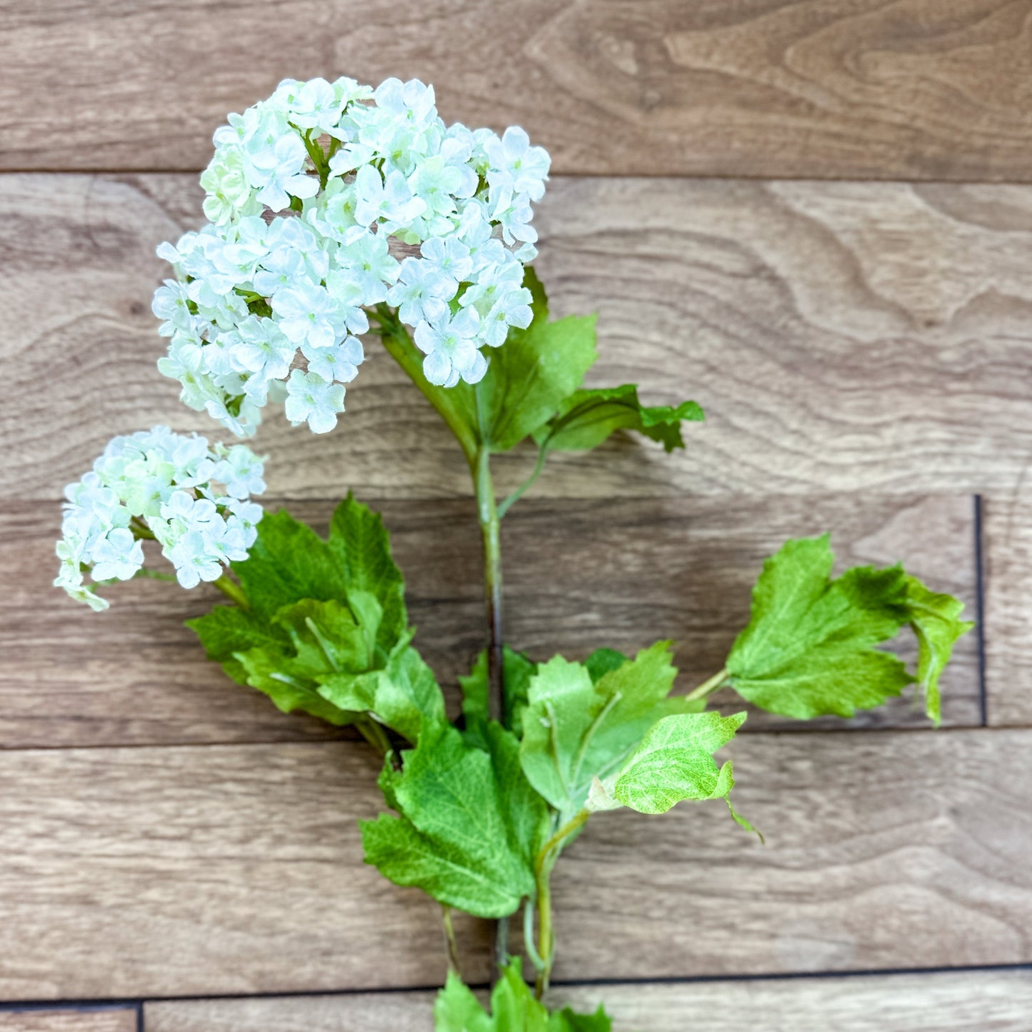 Artificial flower branch with white flowers and green leaves on a wooden surface 32" White Snowball 2 Bloom Hydrangea Stem Spray