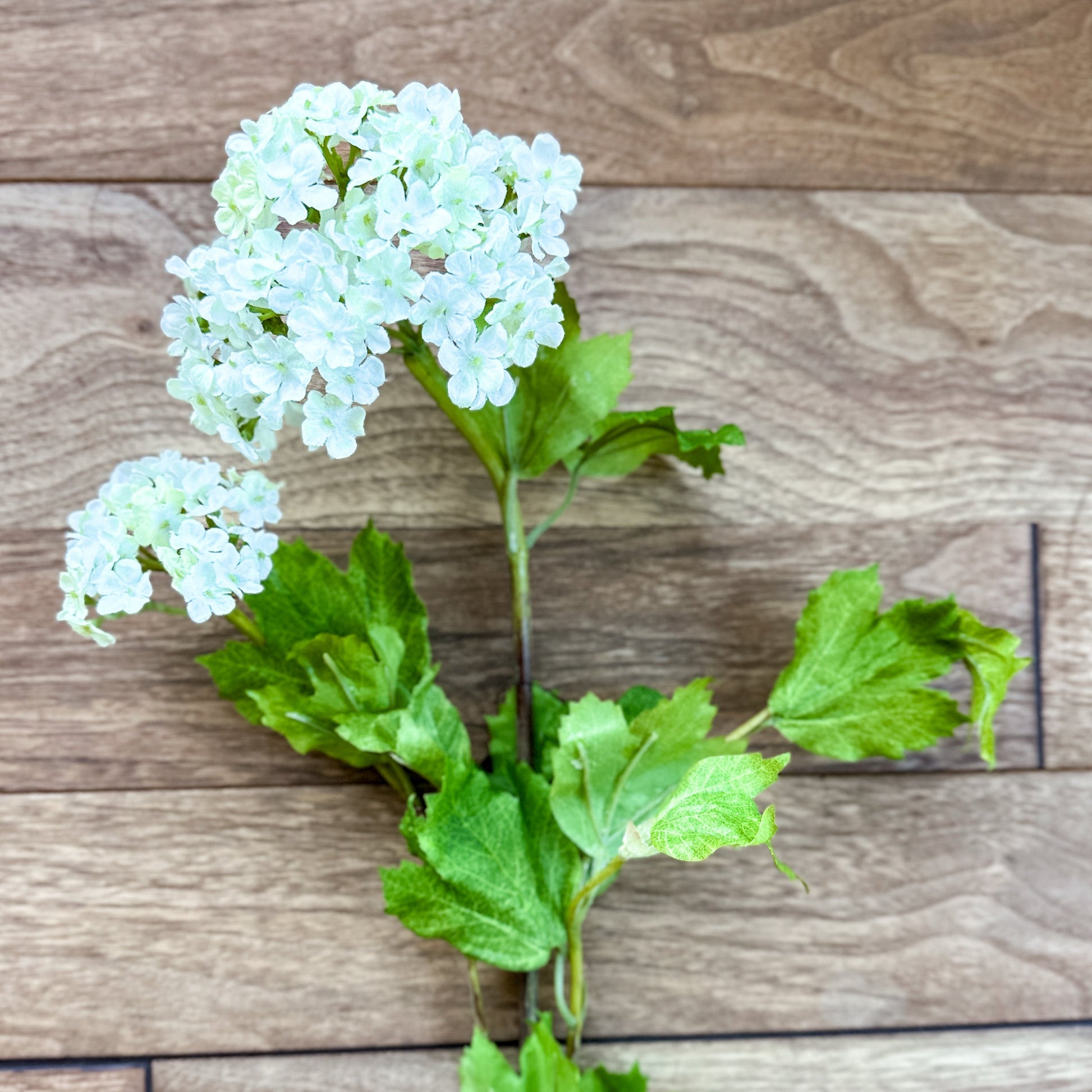 Artificial flower branch with white flowers and green leaves on a wooden surface 32" White Snowball 2 Bloom Hydrangea Stem Spray