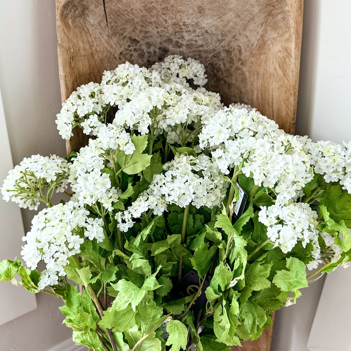 White flowers and green leaves on a wooden chair against a white wall