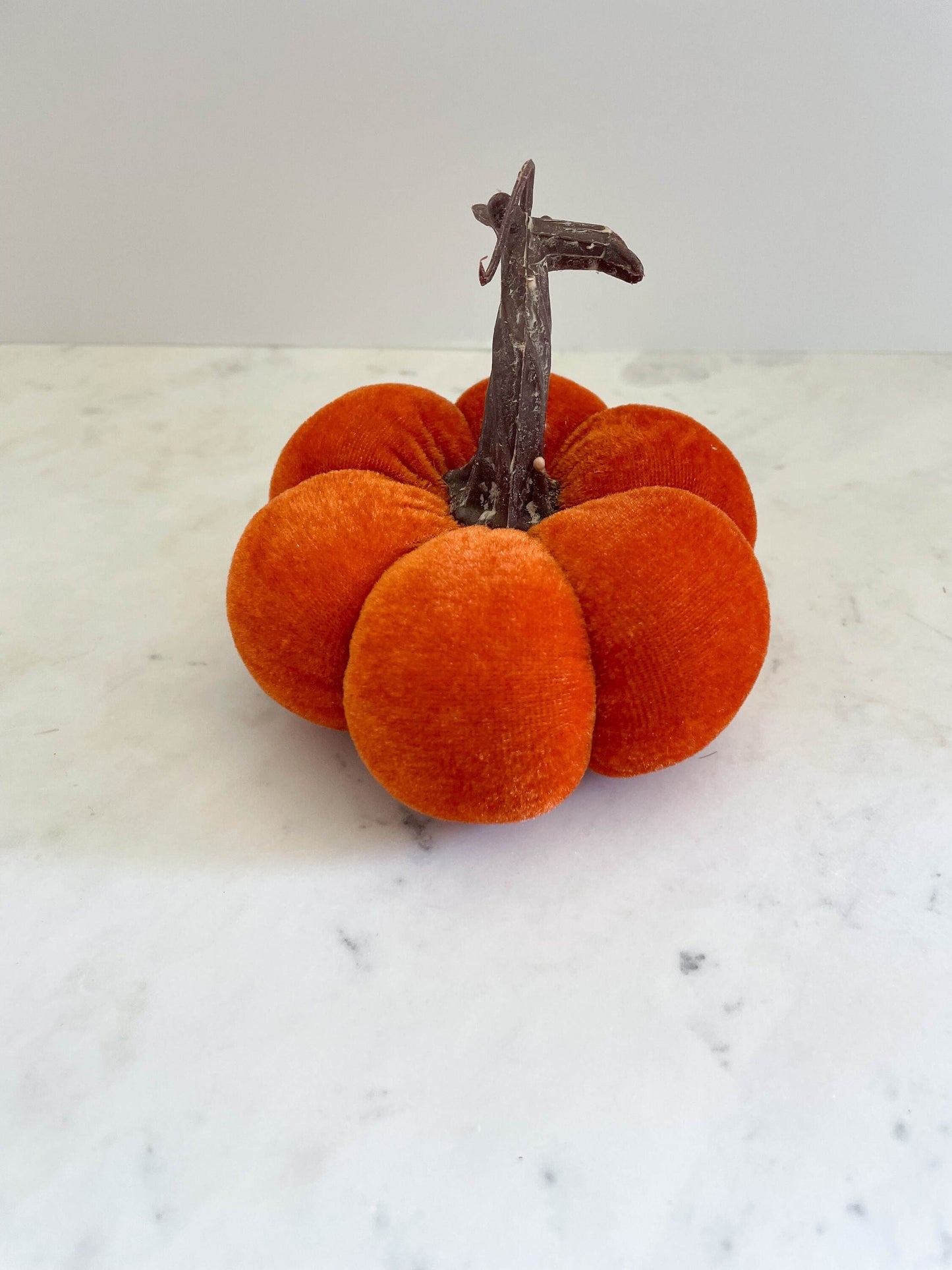 A 3-inch orange velvet pumpkin with a brown stem, placed on a marble surface.