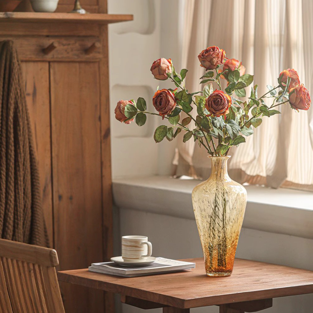 Decorative vase with flowers on a wooden table next to a chair and a cabinet.
