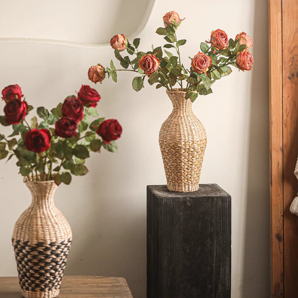 Two woven vases with artificial rose flowers on a wooden surface.