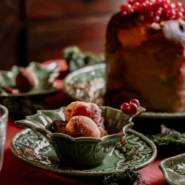 Decorative table setting with green plates, red berries, and a loaf of bread on a wooden surface.