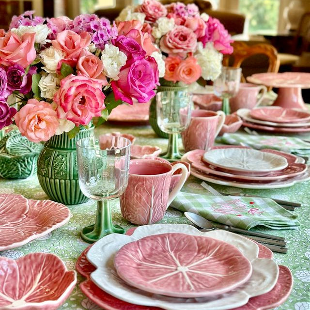 Decorative table setting with pink floral arrangements, dishes, and glasses on a green tablecloth.