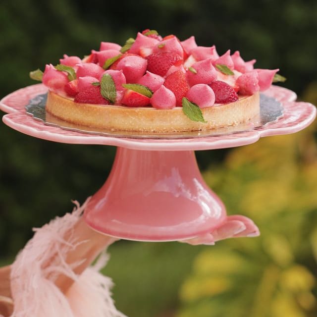 Pink cake stand with a strawberry tart on a blurred green background
