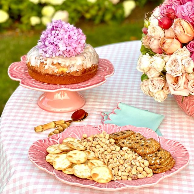 Table with cookies, crackers, and a cake on a checkered tablecloth outdoors.