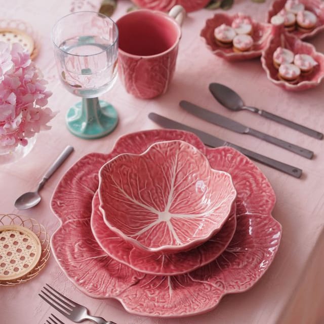 Pink ceramic cabbage leaf-patterned dishes on a table with silverware and glasses.