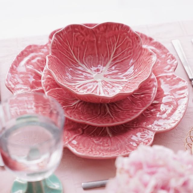 Set of pink ceramic plates with cabbage leaf patterns on a light pink tablecloth.
