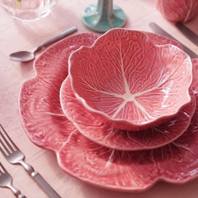 Pink cabbage leaf-patterned dinnerware set on a table with floral decorations.