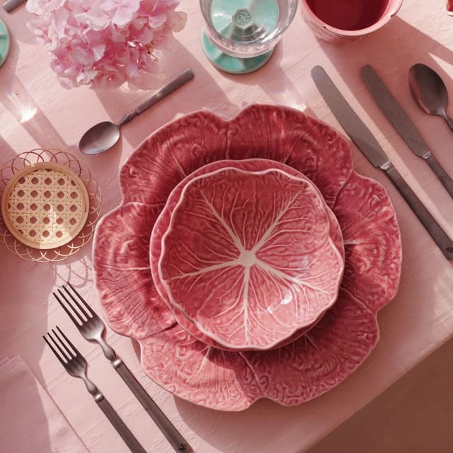 Pink floral dinnerware set on a matching pink tablecloth with silverware and flowers.