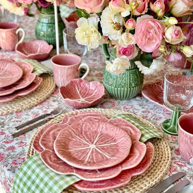 Colorful table setting with pink cabbage dishes, flowers, and green vases.