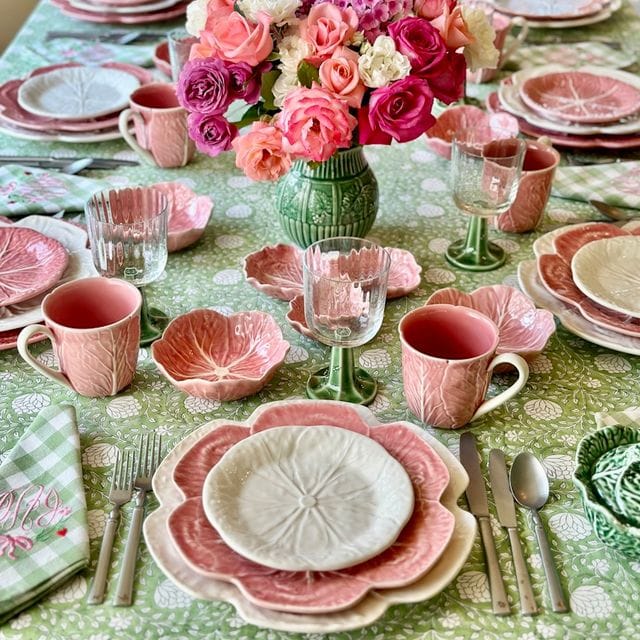 Dining table set with pink and green tableware, floral centerpieces, and cutlery.