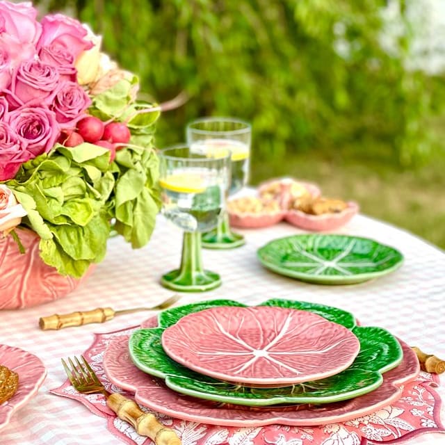 Outdoor table setting with pink and green plates, glasses, and flowers.