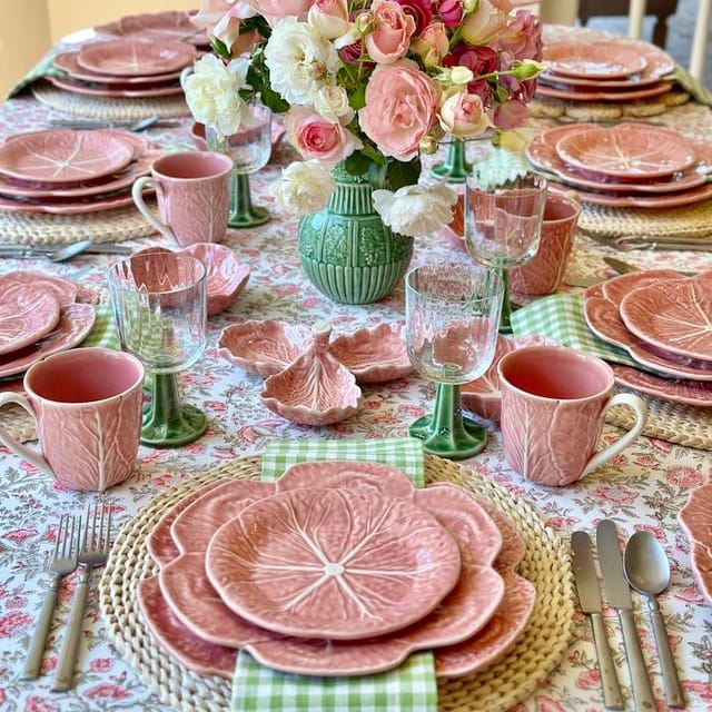 Dining table set with pink ceramic plates, cups, and floral centerpieces.