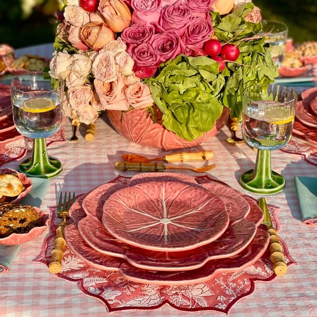 Decorative table setting with floral centerpiece, pink plates, and green glasses.