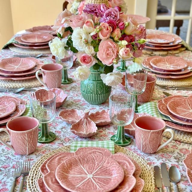 Dining table set with pink ceramic plates, cups, and floral centerpieces.
