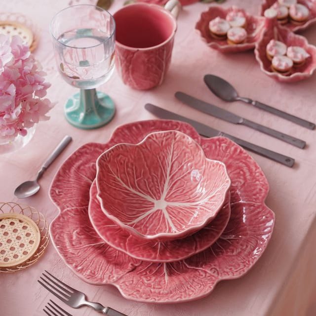 Pink ceramic cabbage-patterned dishes on a table with silverware and glasses.