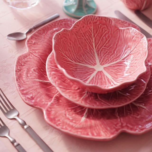 Pink cabbage-patterned dinnerware set on a table with floral decorations.