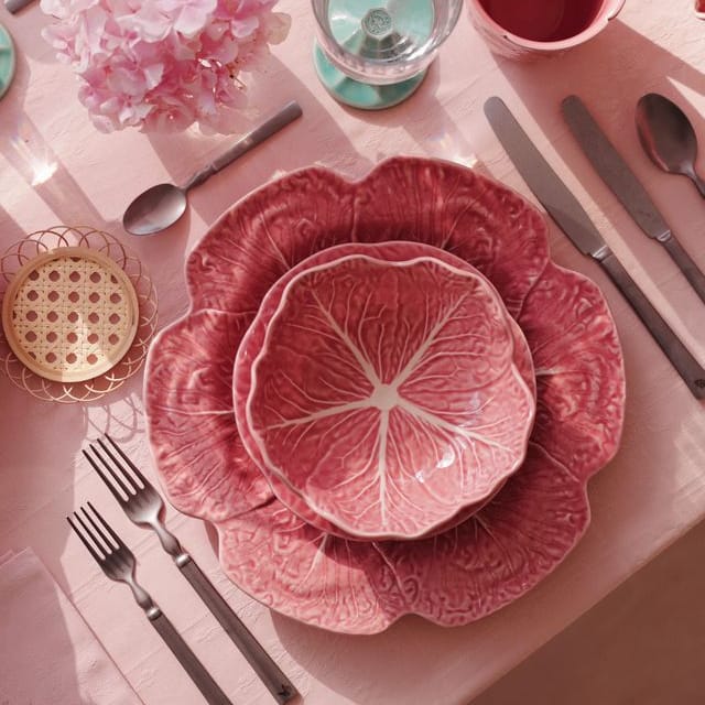 Pink floral dinnerware set on a matching pink tablecloth with silverware and flowers.