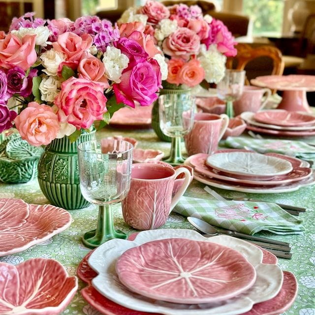 Decorative table setting with pink floral arrangements, plates, and glasses on a green tablecloth.