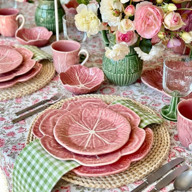 Colorful table setting with pink plates, flowers, and green vases.