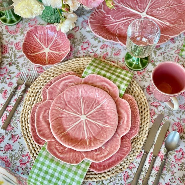 Decorative table setting with pink floral plates, flowers, and cutlery on a patterned tablecloth.