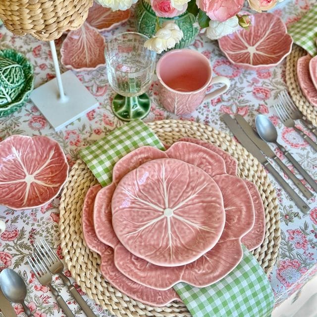 Decorative table setting with pink floral plates, flowers, and cutlery on a patterned tablecloth.