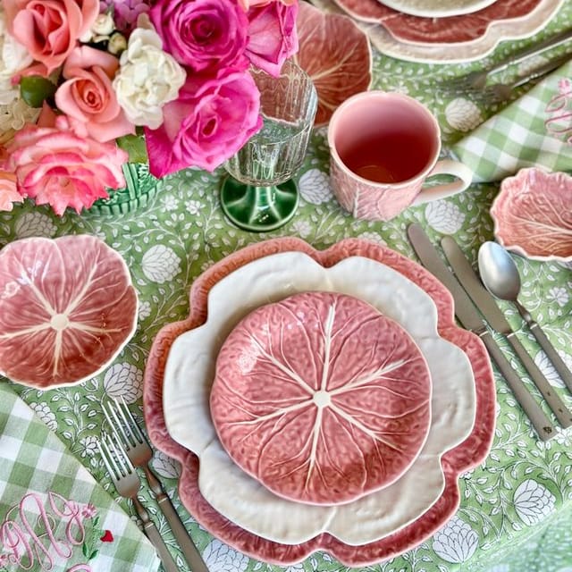 Decorative table setting with pink floral arrangement, plates, and cutlery on a checkered tablecloth.