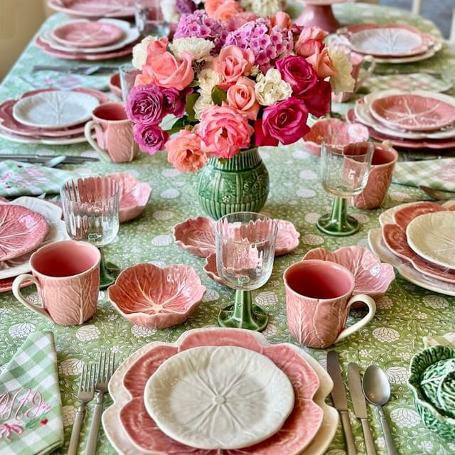 Dining table set with pink and green tableware, floral centerpieces, and cutlery.