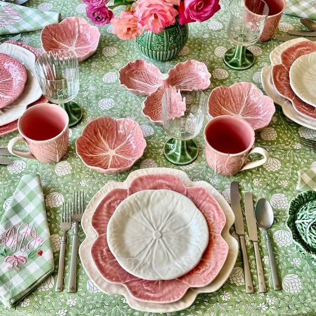 Decorative table setting with pink floral plates, cups, and a centerpiece on a green patterned tablecloth.