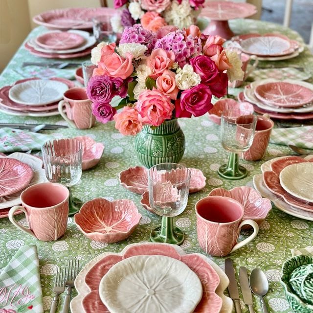 Dining table set with pink and green tableware, floral centerpieces, and cutlery.